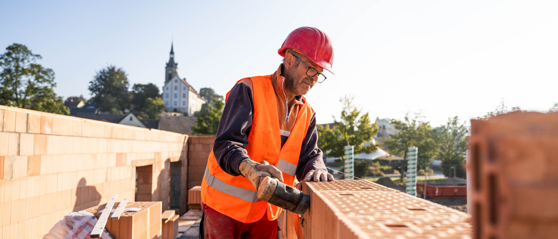 Mann in Arbeitskleidung legt einen Ziegelstein auf eine Mauer.