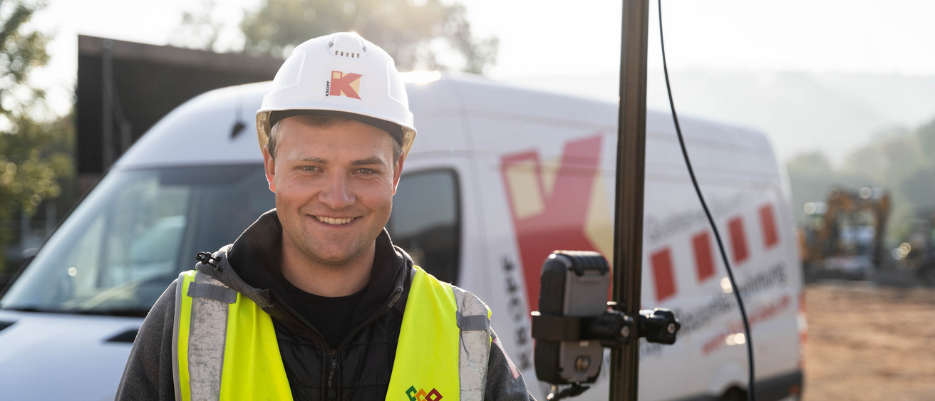 Mann hält einen Vermessungsstab auf einer Baustelle.